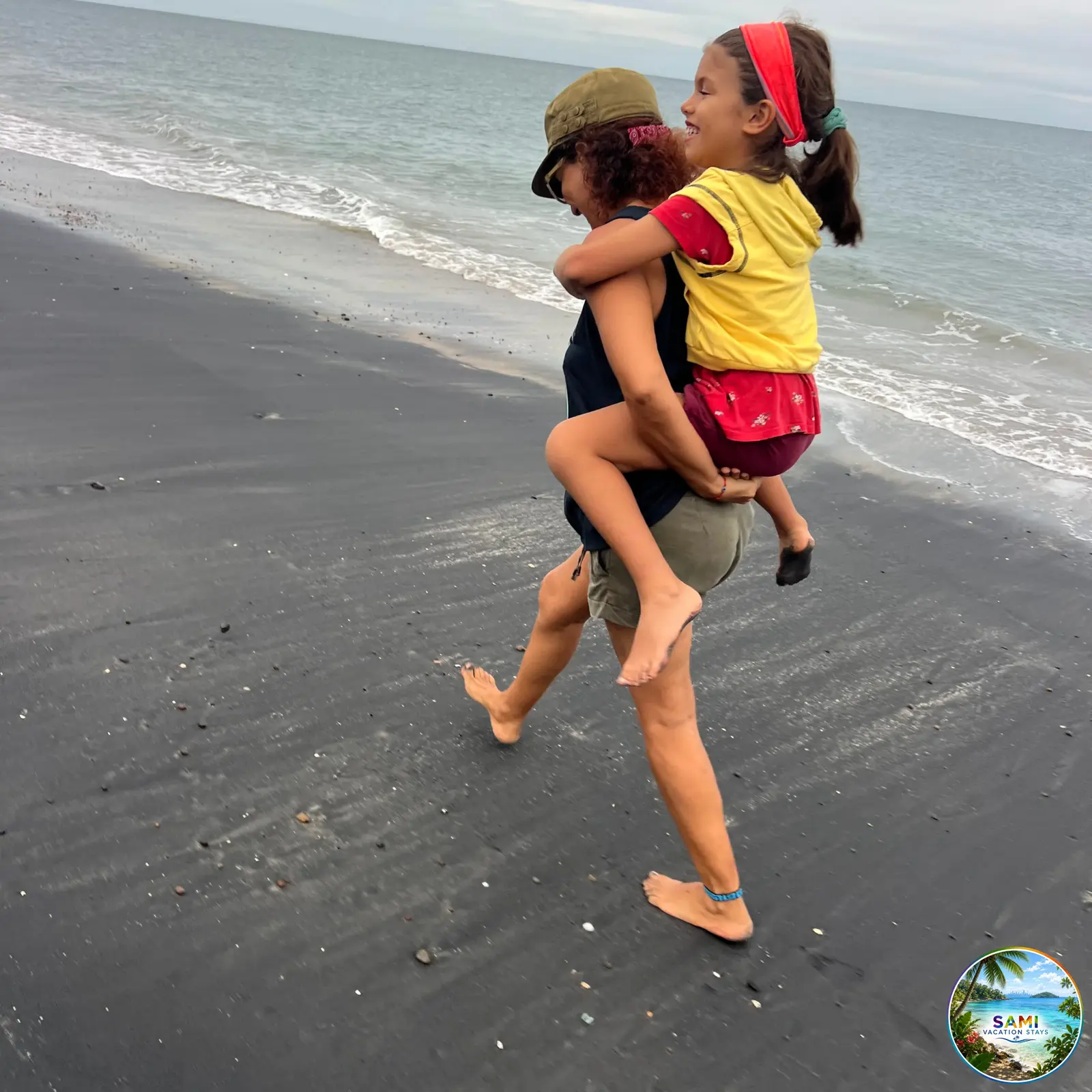 Mother carrying a child piggyback on a black sand beach